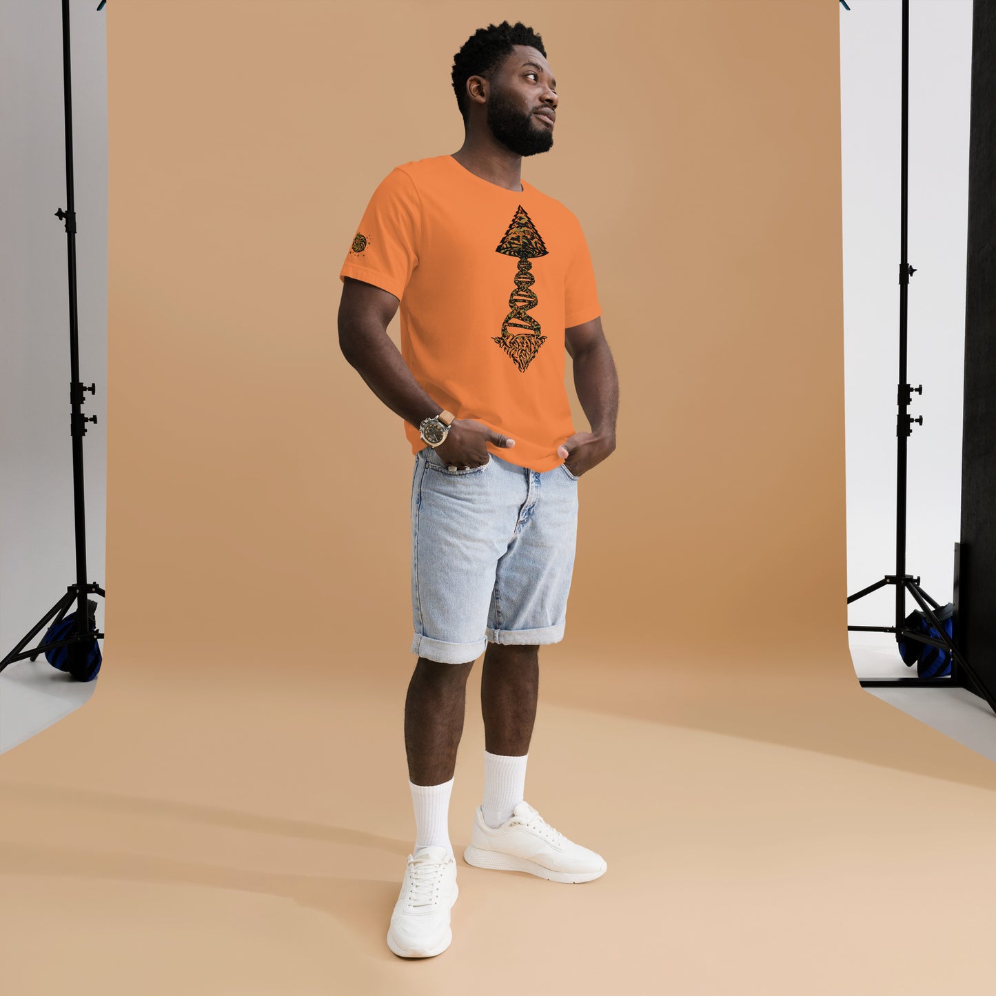 Man wearing an orange Tango Tree Of Life t-shirt, styled with denim shorts and sneakers, posing against a neutral backdrop.
